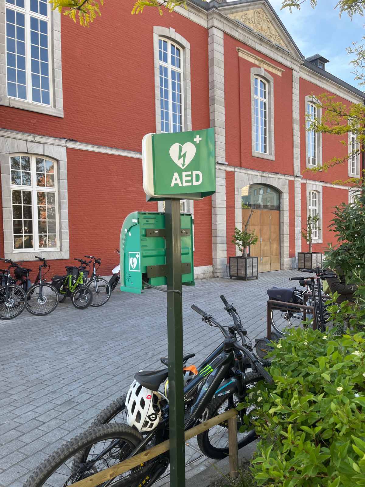 AED In het perkje tussen stadhuis en fonteinen, bevestigd aan een paal, links van Infotoerisme