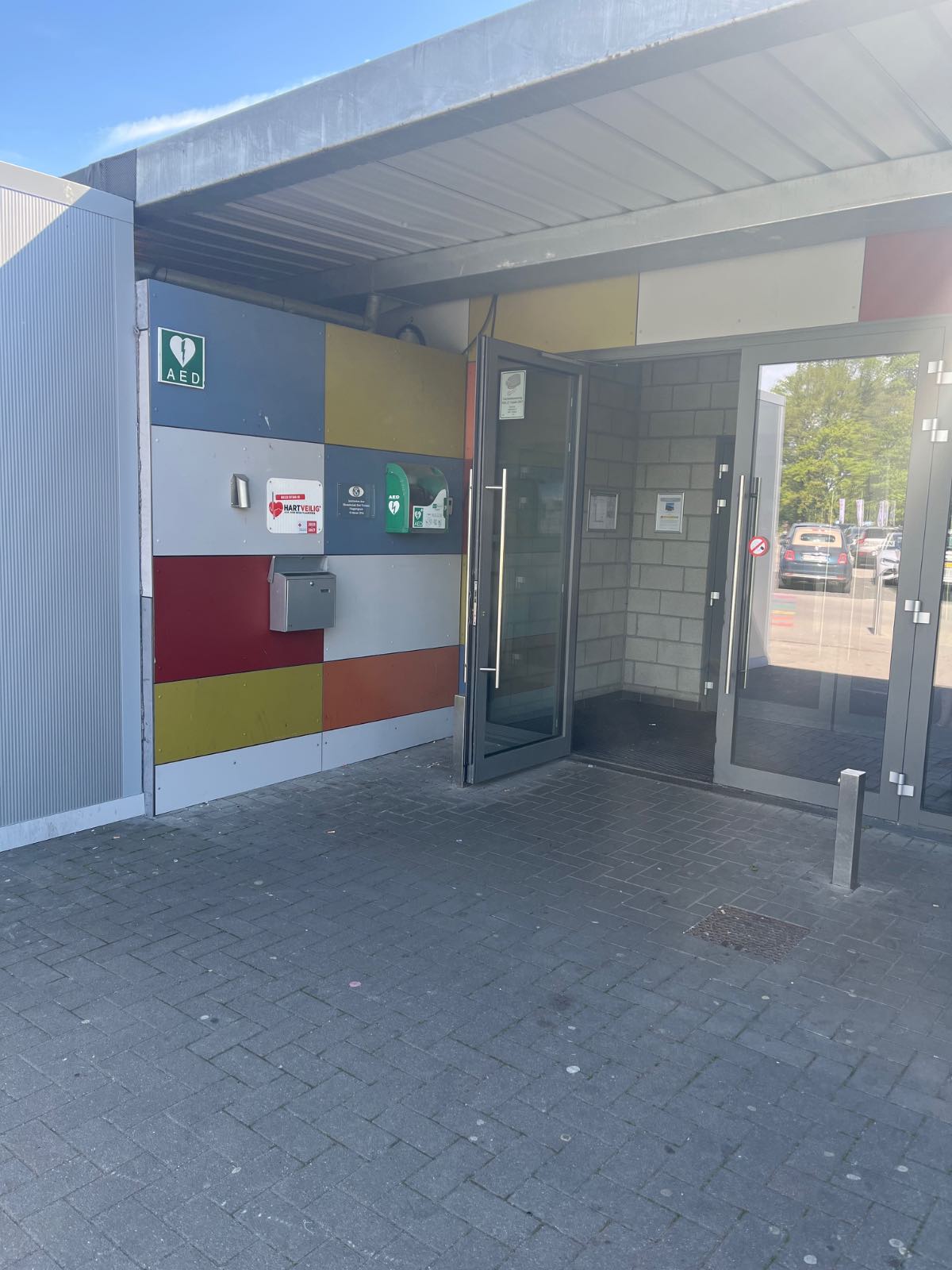 AED Buiten links van de inkom van de sporthal - altijd bereikbaar rijden tot op 10m van deur mogelijk