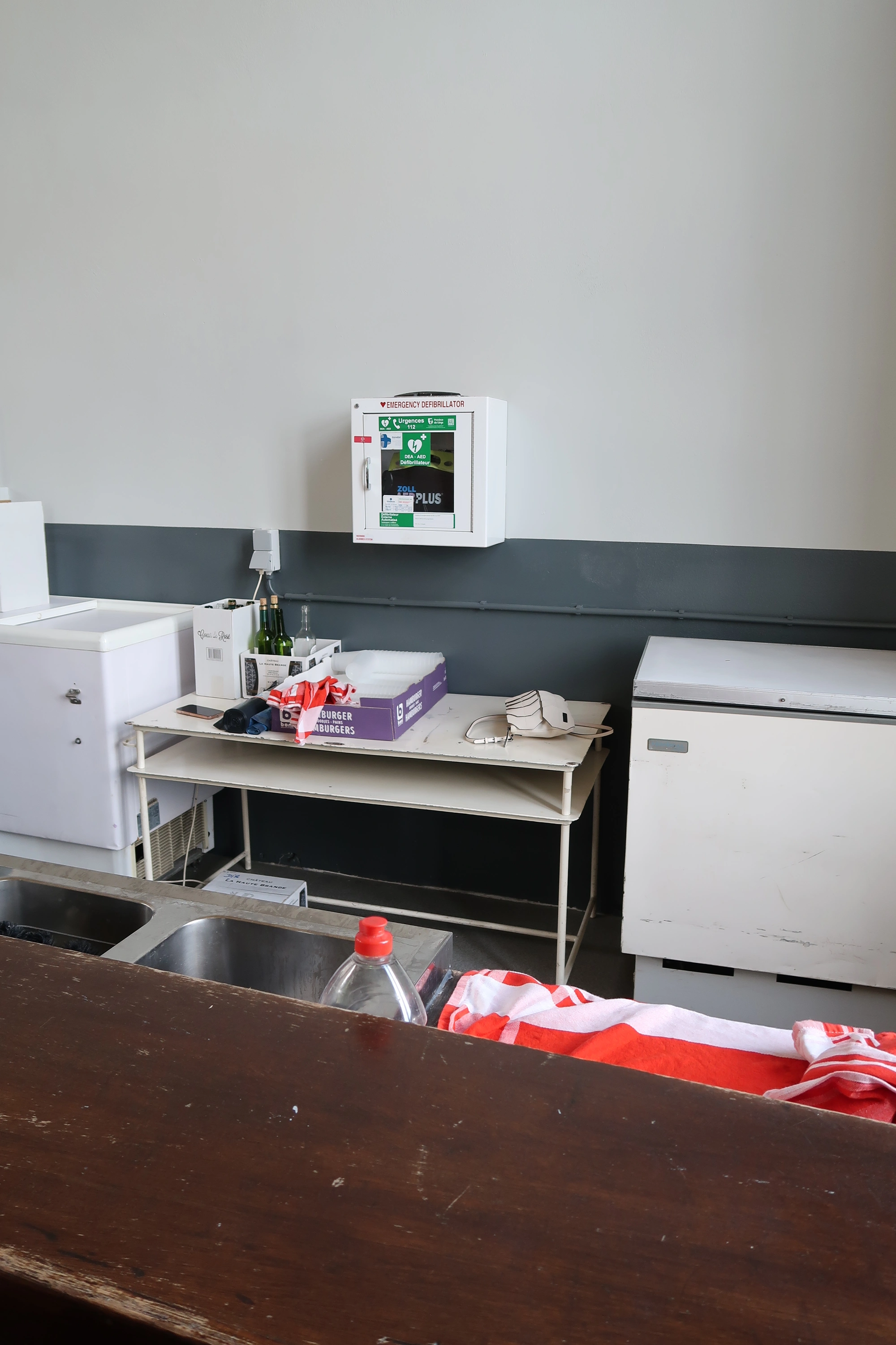 AED In zaal Gymnase, achter de toog; toegankelijk tijdens activiteiten