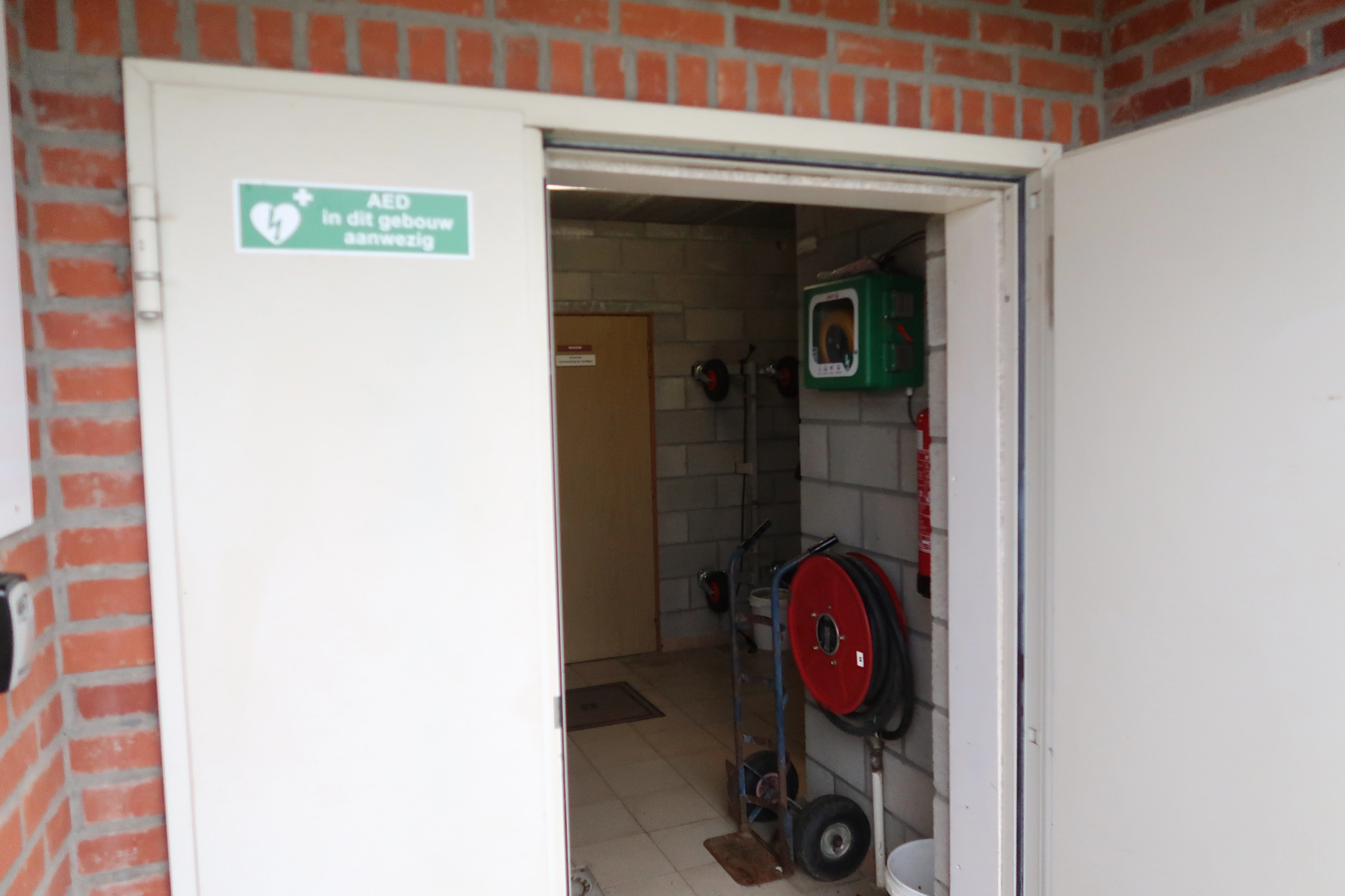 AED Binnen in het halletje van de kleedkamers, ingang aan de kant van het voetbalterrein