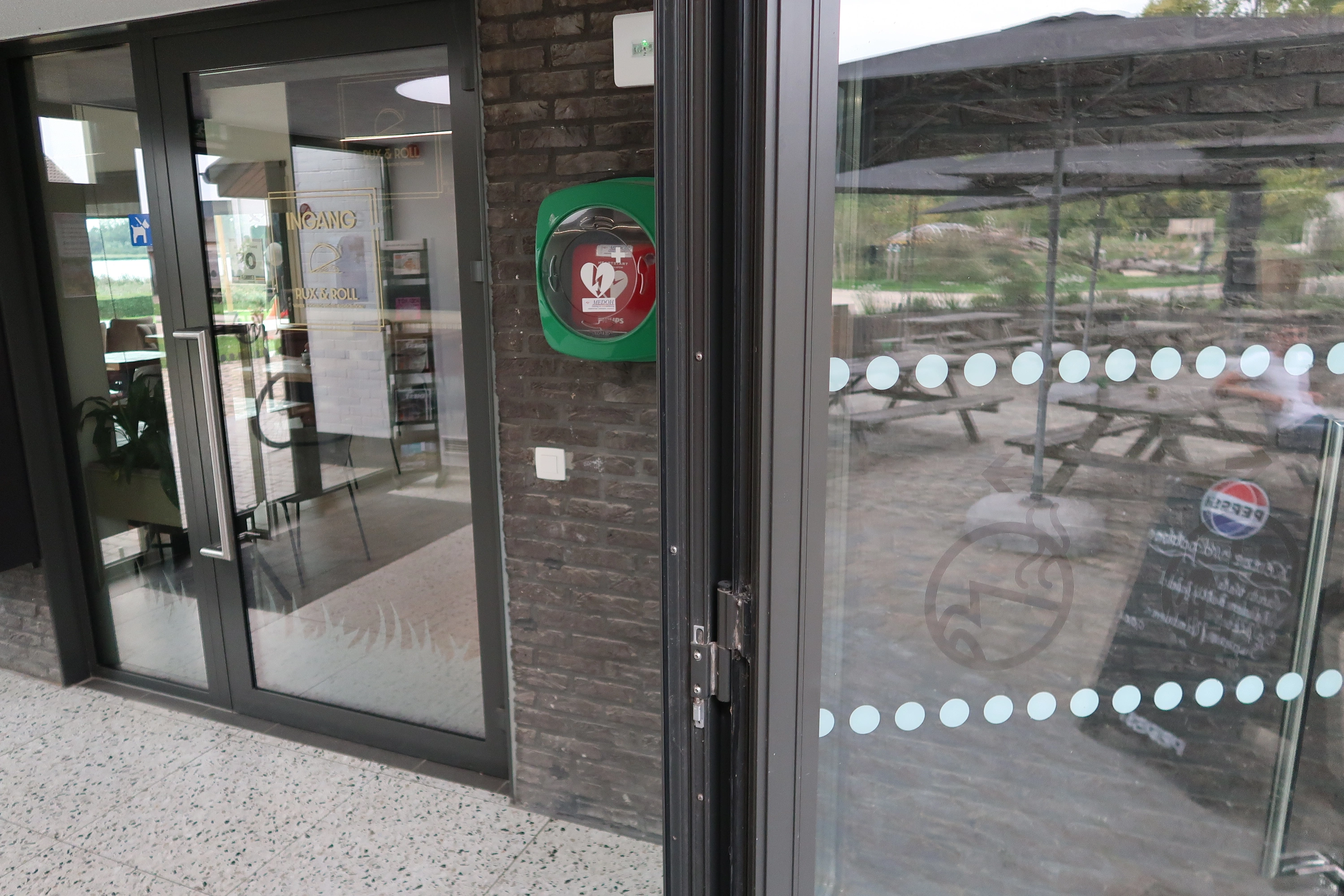 AED In de hal tussen bistro en de WC, zichtbaar van buiten.