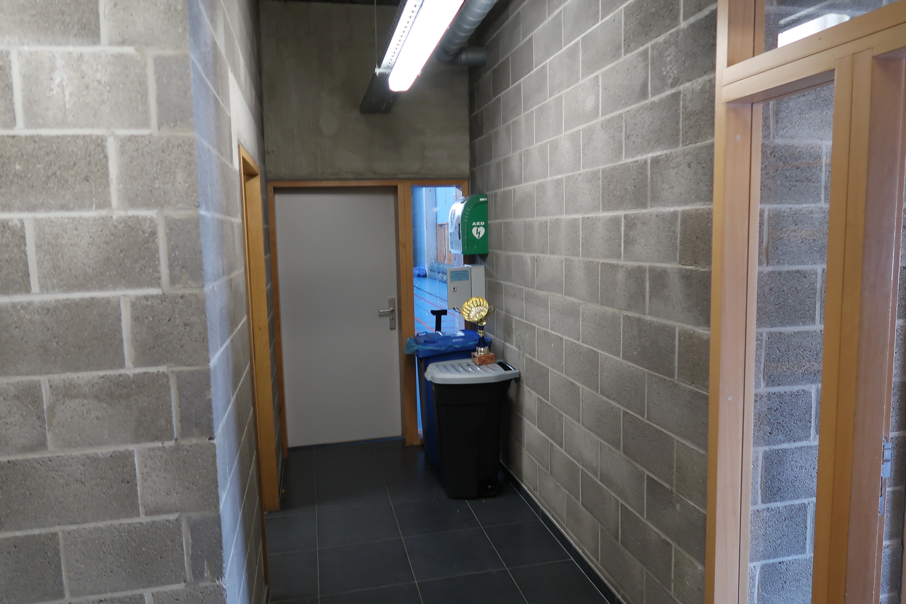 AED Naast de sportzaal van de school, achter de deur naar de kleedkamers en toiletten