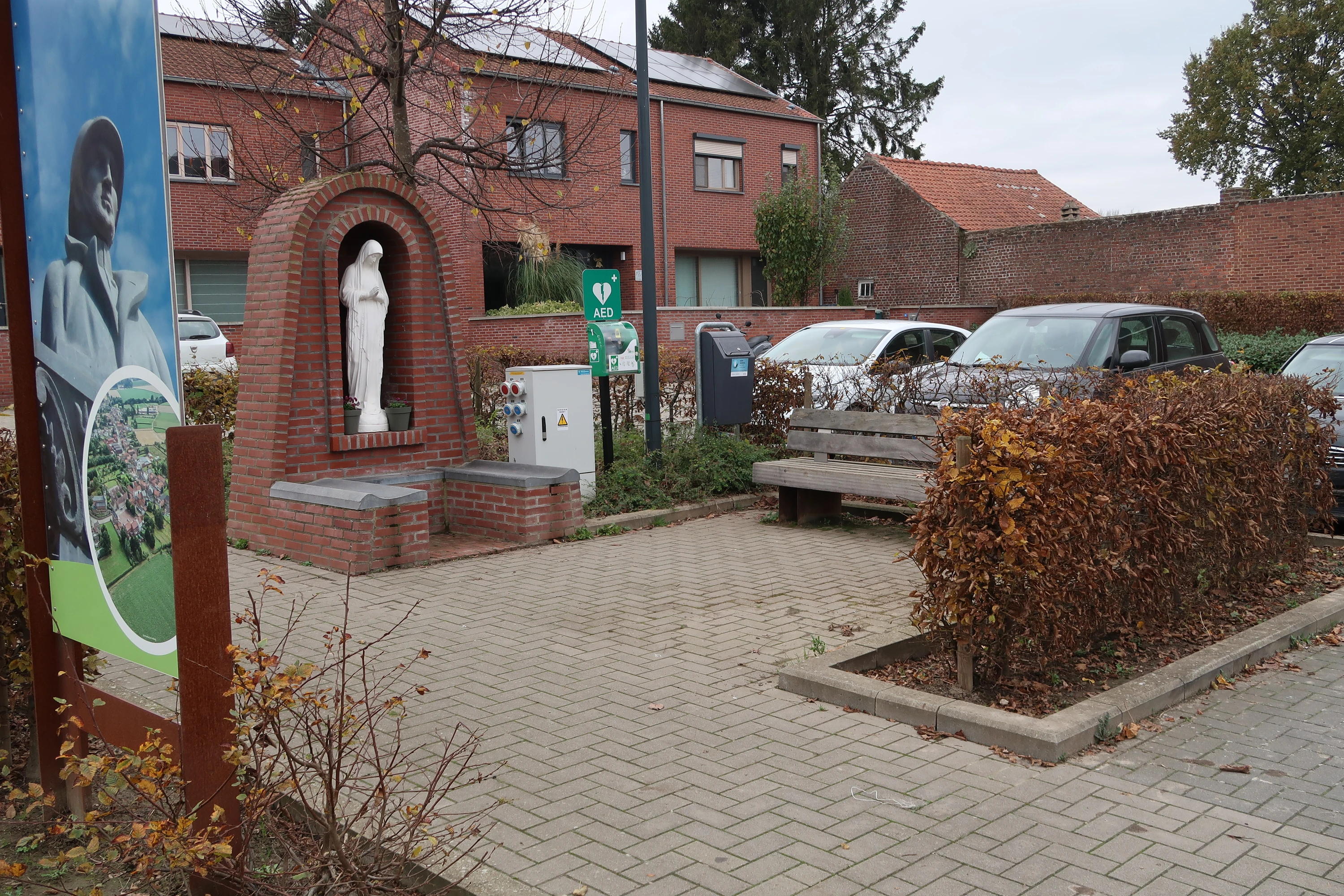 AED Buiten in het midden van het pleintje, rechts van het kapelletje