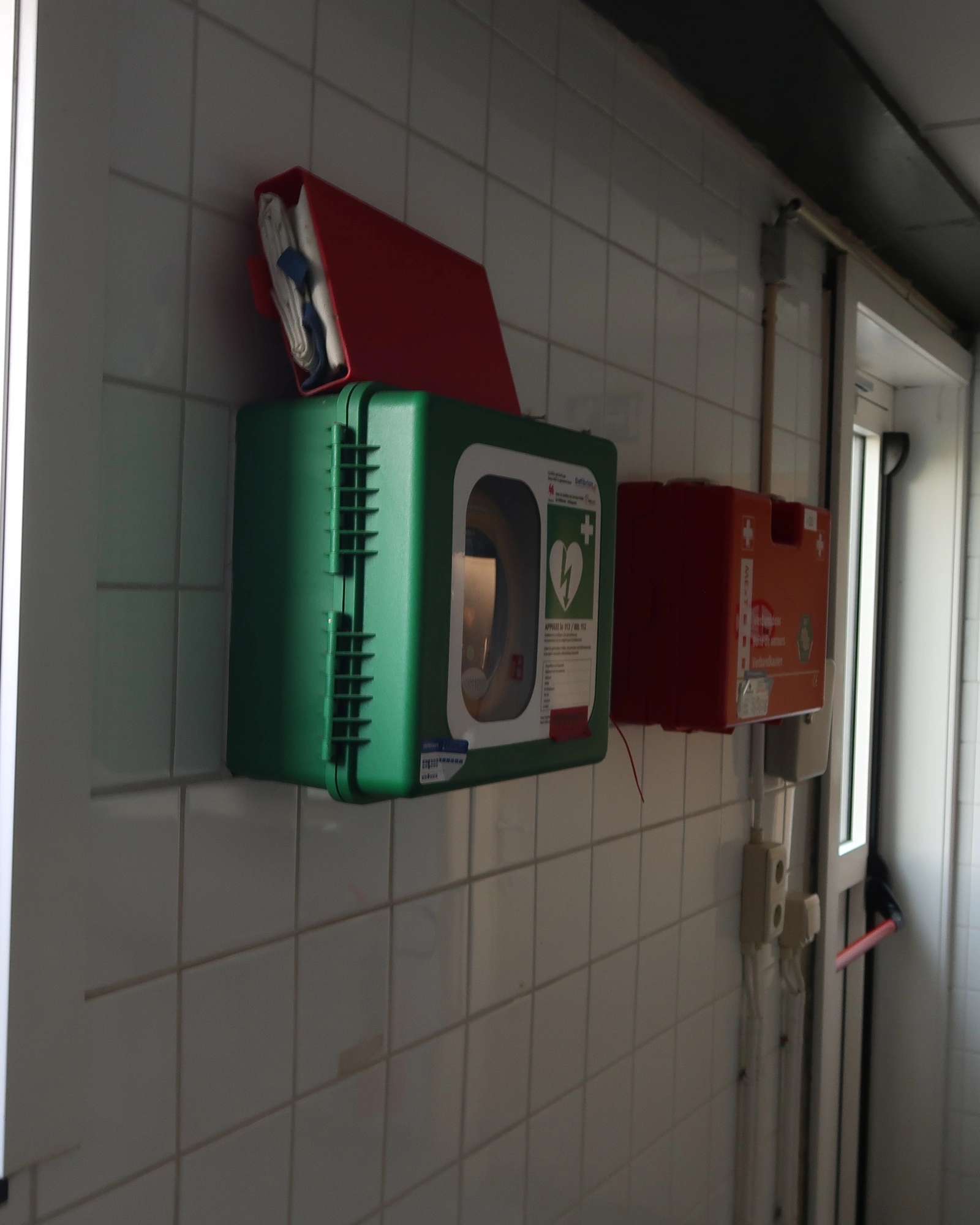 AED In de keuken tegen de buitenmuur van de zaal van Marilles, toegankelijk tijdens activiteiten in de zaal