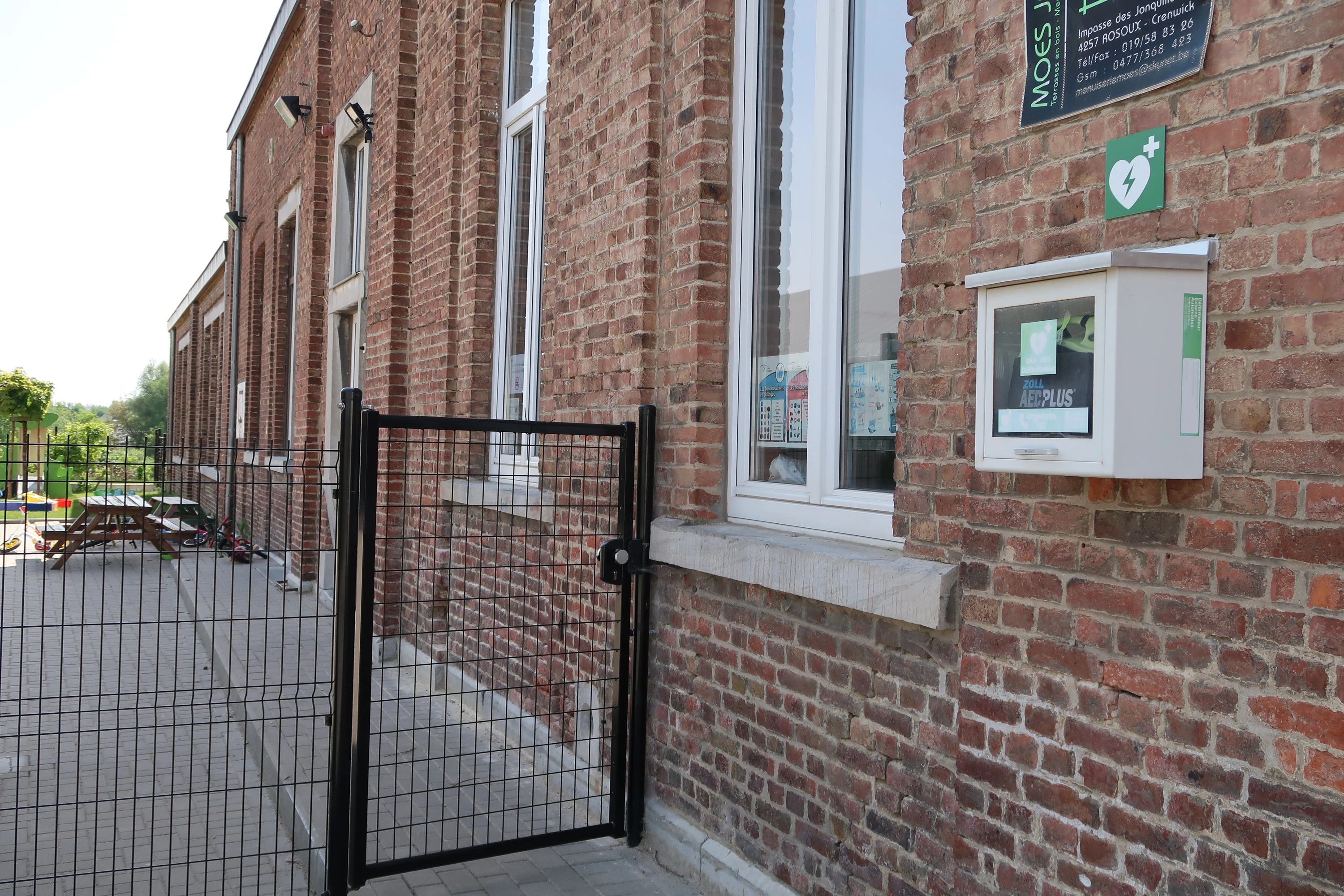 AED Contre la façade de l'école, à côté de la porte d'accès à la cour de récréation