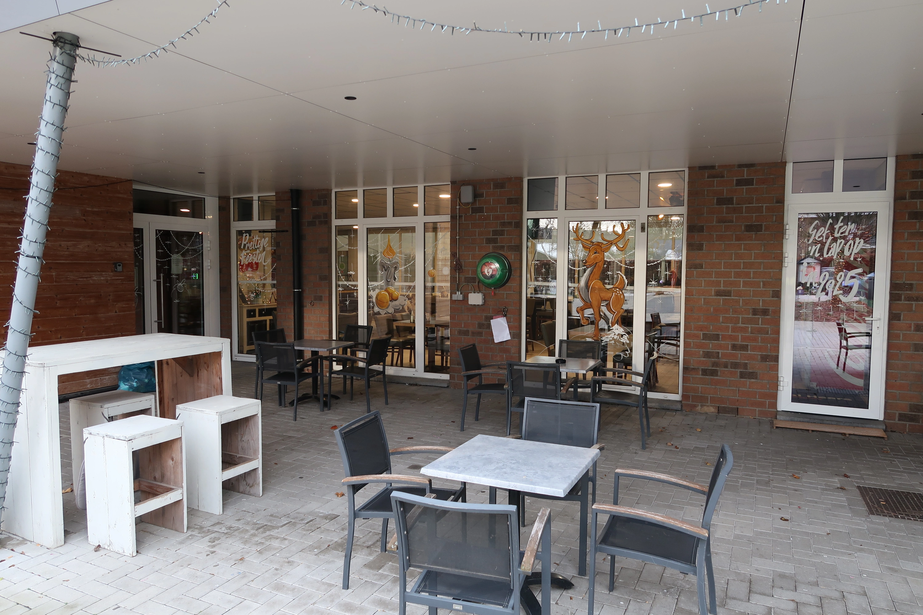 AED Buiten onder het afdak van het terras van het cafetaria, naast de ingang