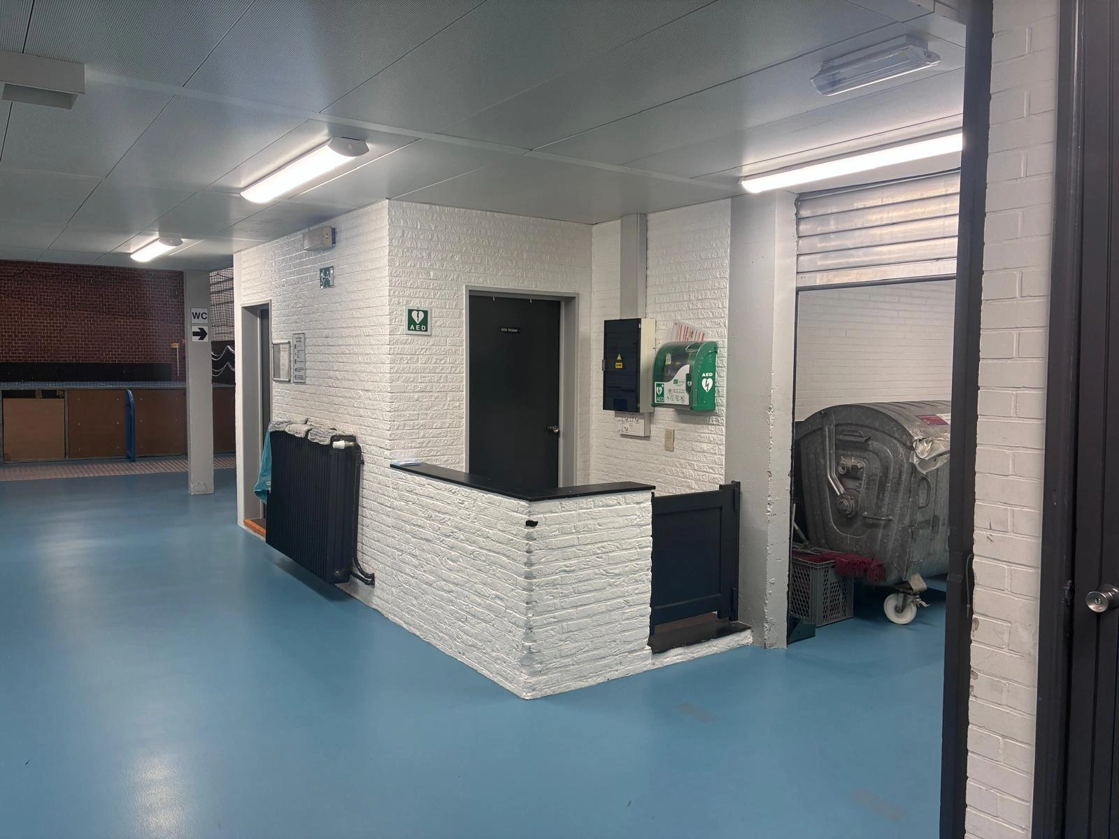 AED Sporthal, binnen in inkomhal aan de rechterkant naast elektriciteitskast