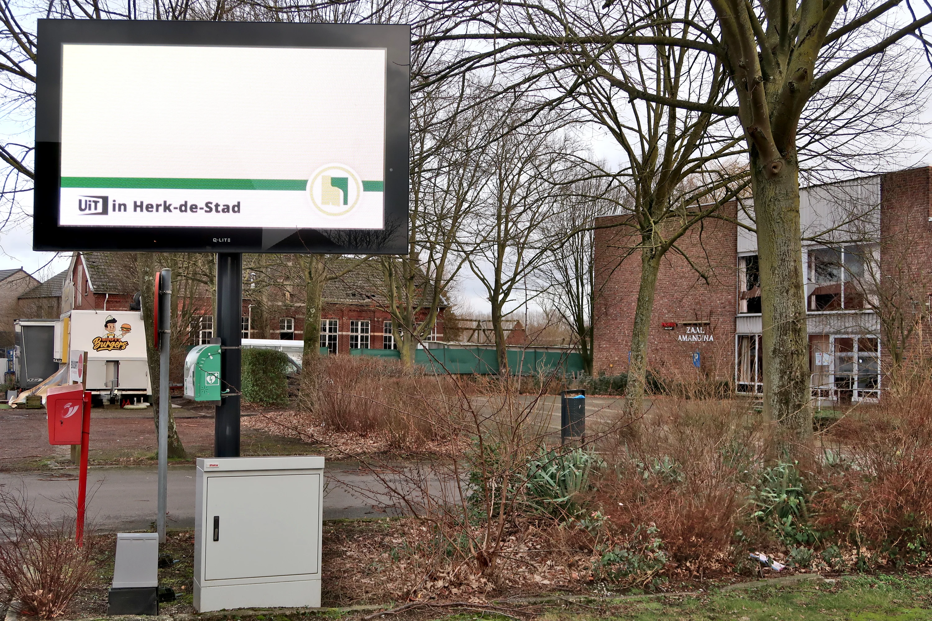 AED Tegen de paal van het infoscherm langs de Schoolstraat, voorbij de kerk