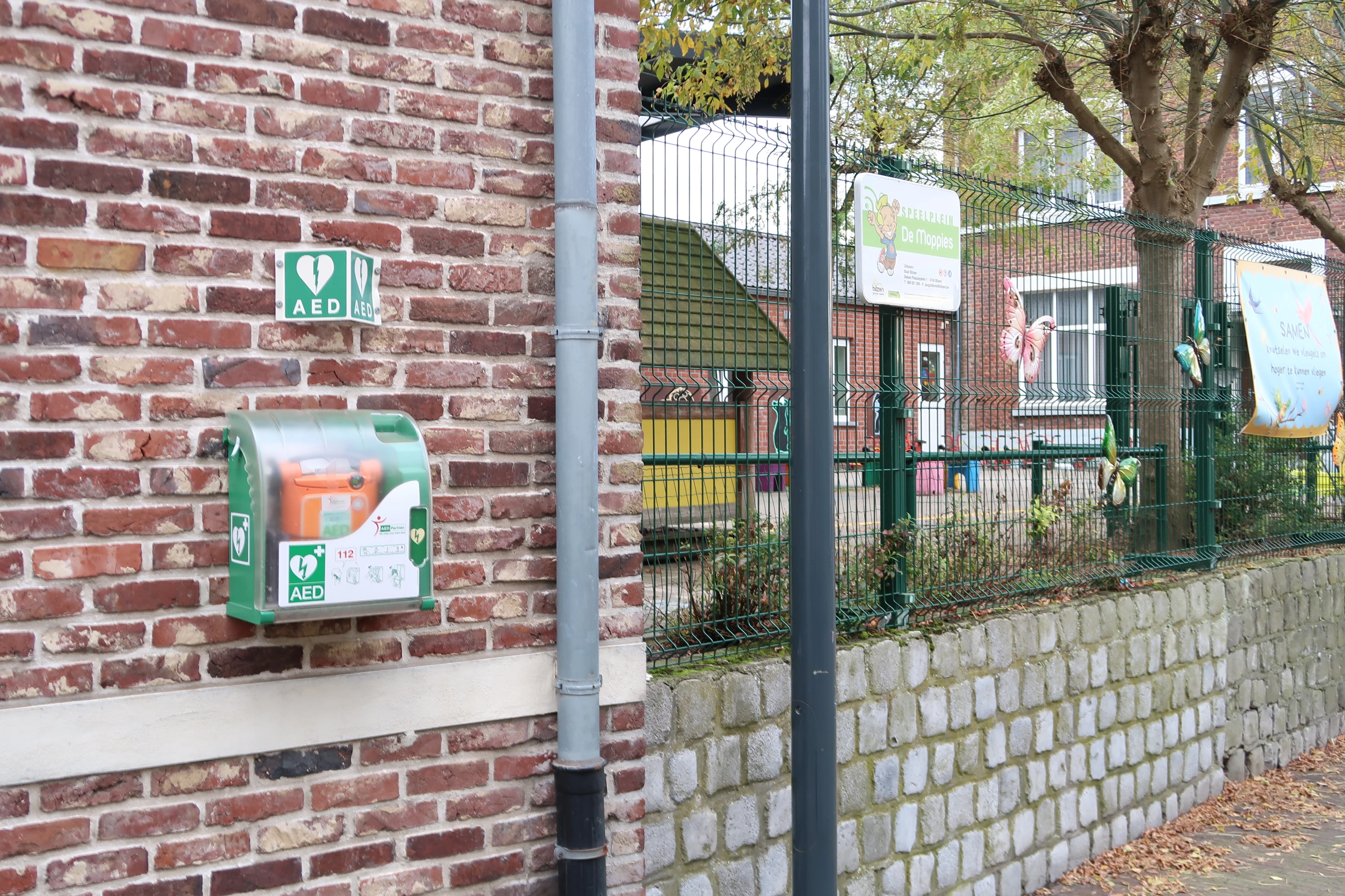 AED Buiten rechts tegen de voorgevel van de basisschool tegenover de kerk